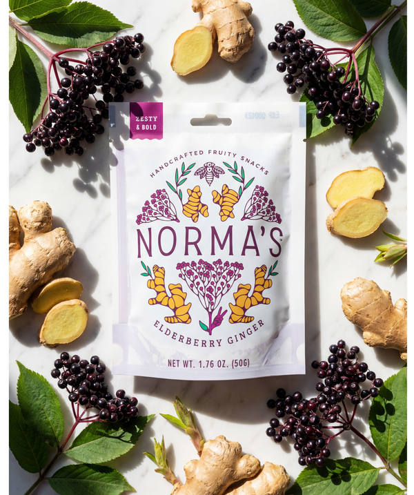 Norma's Elderberry Ginger fruit snacks package surrounded by fresh ingredients on a white background