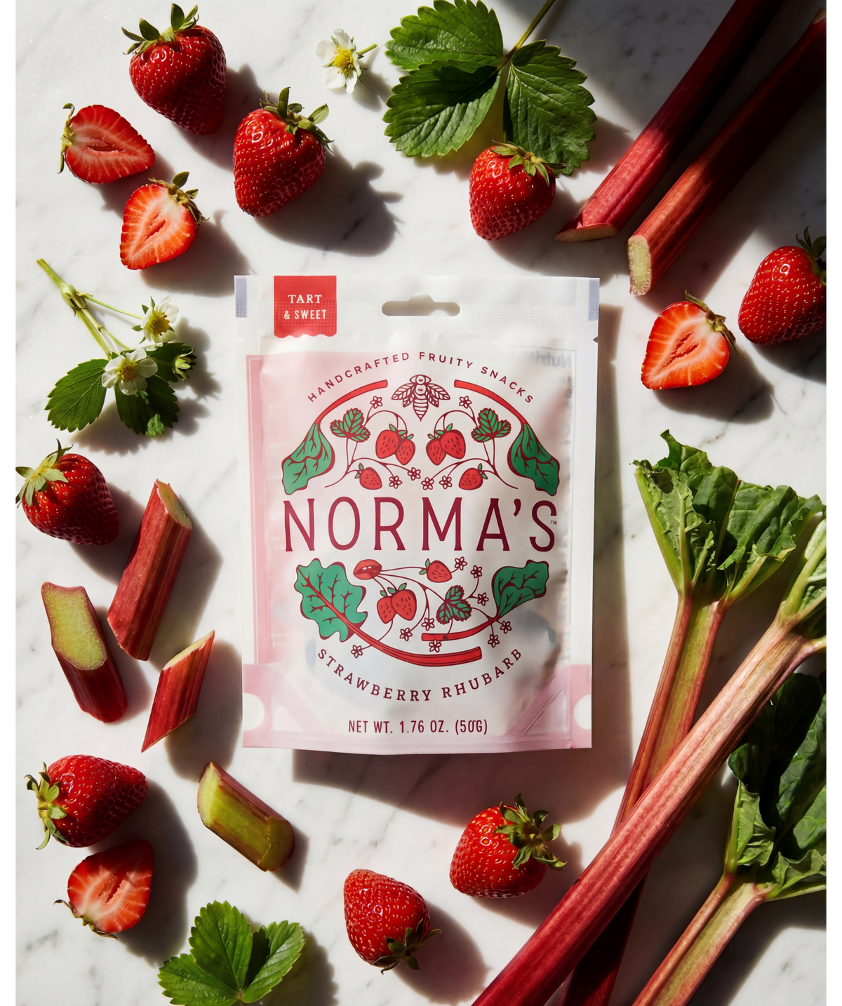 Norma's strawberry rhubarb fruit snack package surrounded by strawberries and rhubarb on a marble surface.
