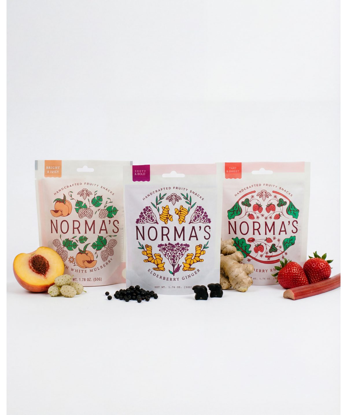 Three packages of 'Norma's' branded snacks on a white background. Peach white mulberry fruit snacks, elderberry ginger fruit snacks, strawberry rhubarb fruit snacks. Real fruit gummies. Made with honey and real fruits and spices.